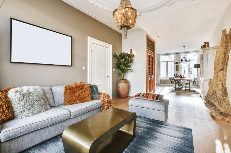 Interior design photography in Washington DC capturing an elegant living room with a neutral palette, modern gray sofa, bold textured pillows, a statement chandelier, and a seamless view into a stylish dining area featuring natural light and ornate details.