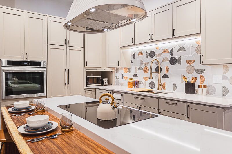 Interior design photography in Washington DC highlighting a chic modern kitchen with warm wood and white finishes, unique geometric backsplash tiles, sleek cabinetry, and a cozy dining setup on the kitchen island.
